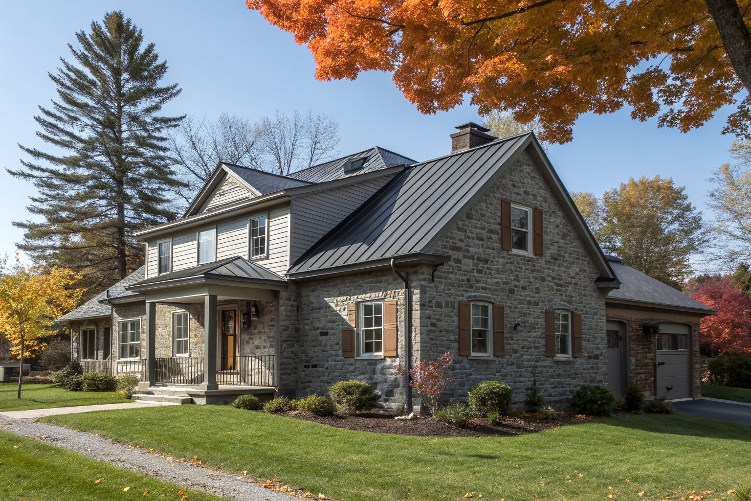 A stone and siding house with a dark standing-seam metal roof, a lawn and autumn trees