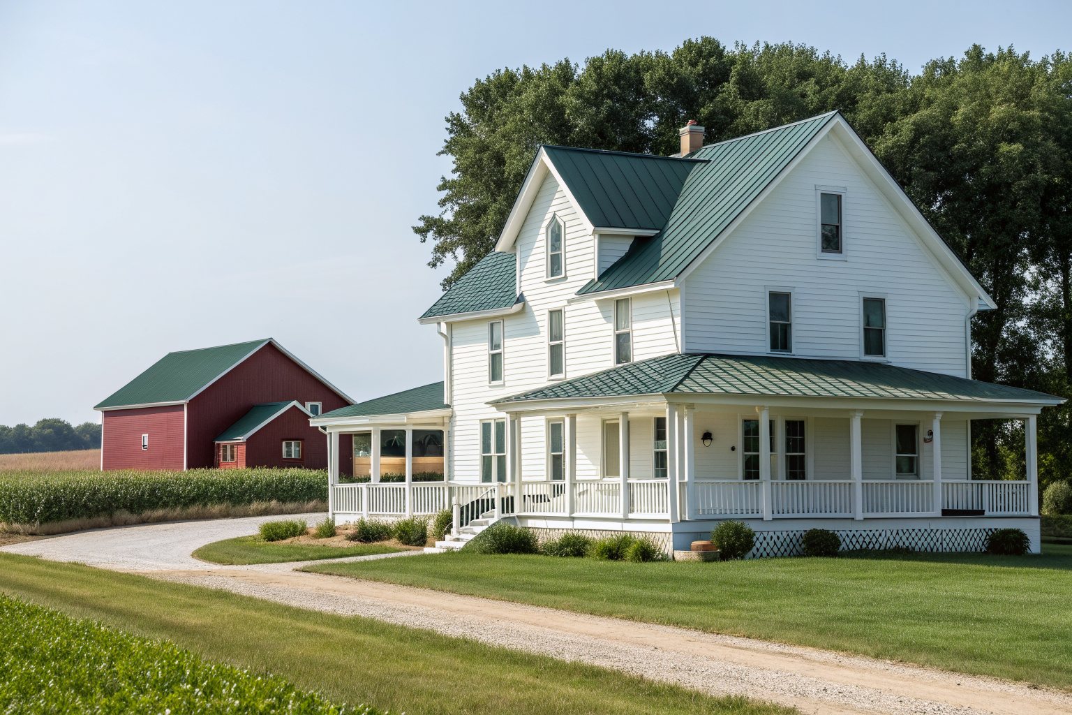A white farmhouse with a green standing-seam metal roof and a wraparound porch beside a red barn and a cornfield